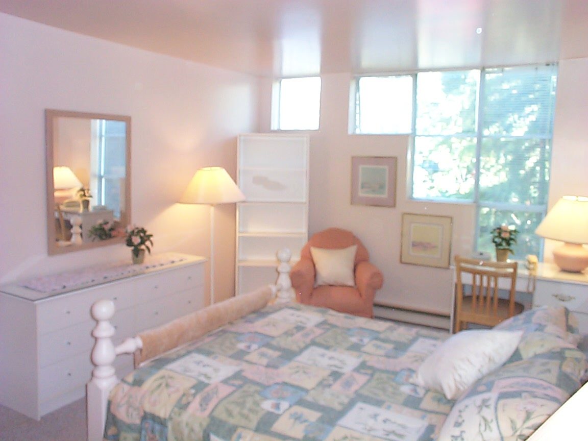 Bright bedroom with large windows, floral bedspread, and wooden furniture. - 832 West 7th Avenue, Vancouver West Side