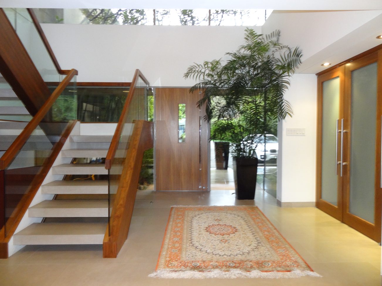 Foyer with modern staircase, glass railings, and a large potted plant. - 2898 Bellevue Avenue, West Vancouver