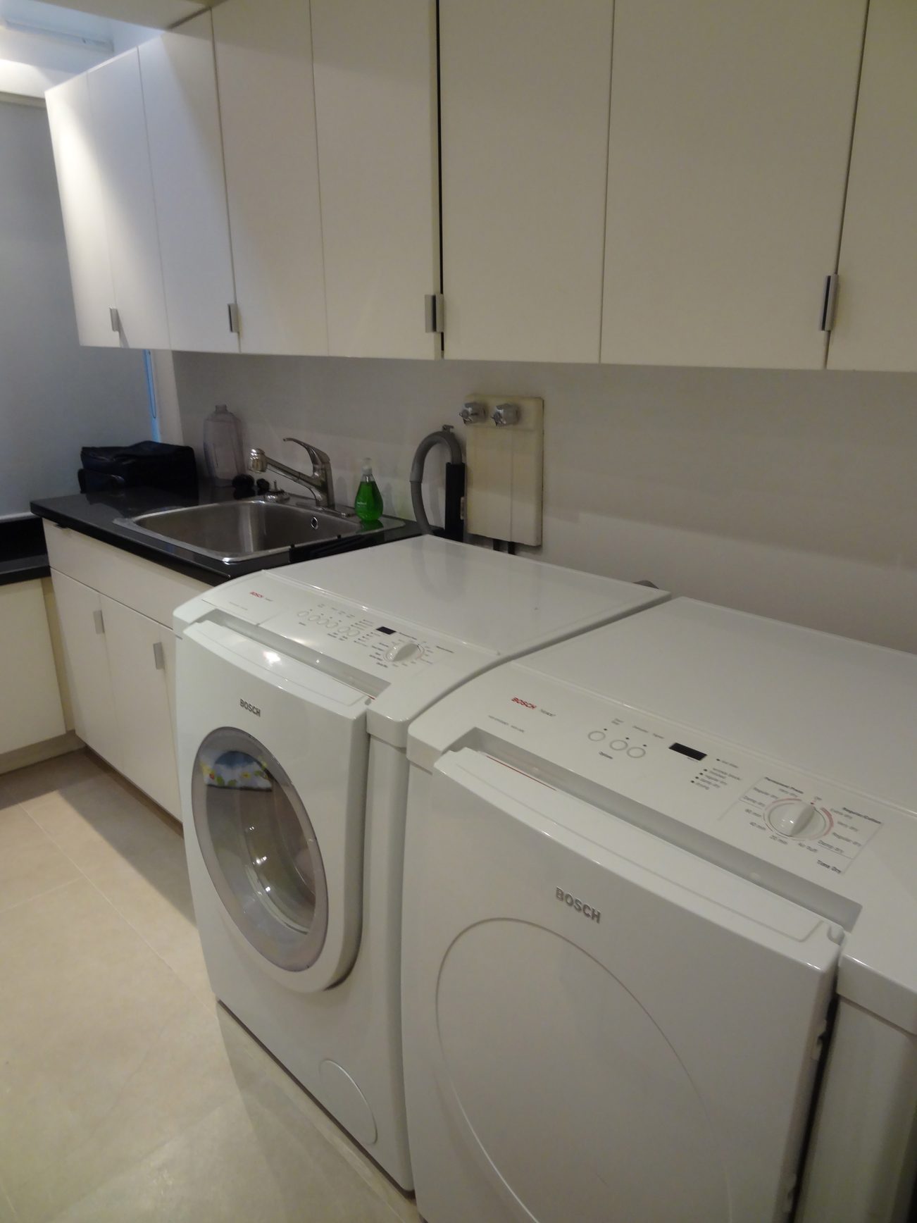 Bright laundry room with Bosch washer and dryer, black countertops, and white cabinets. - 2898 Bellevue Avenue, West Vancouver