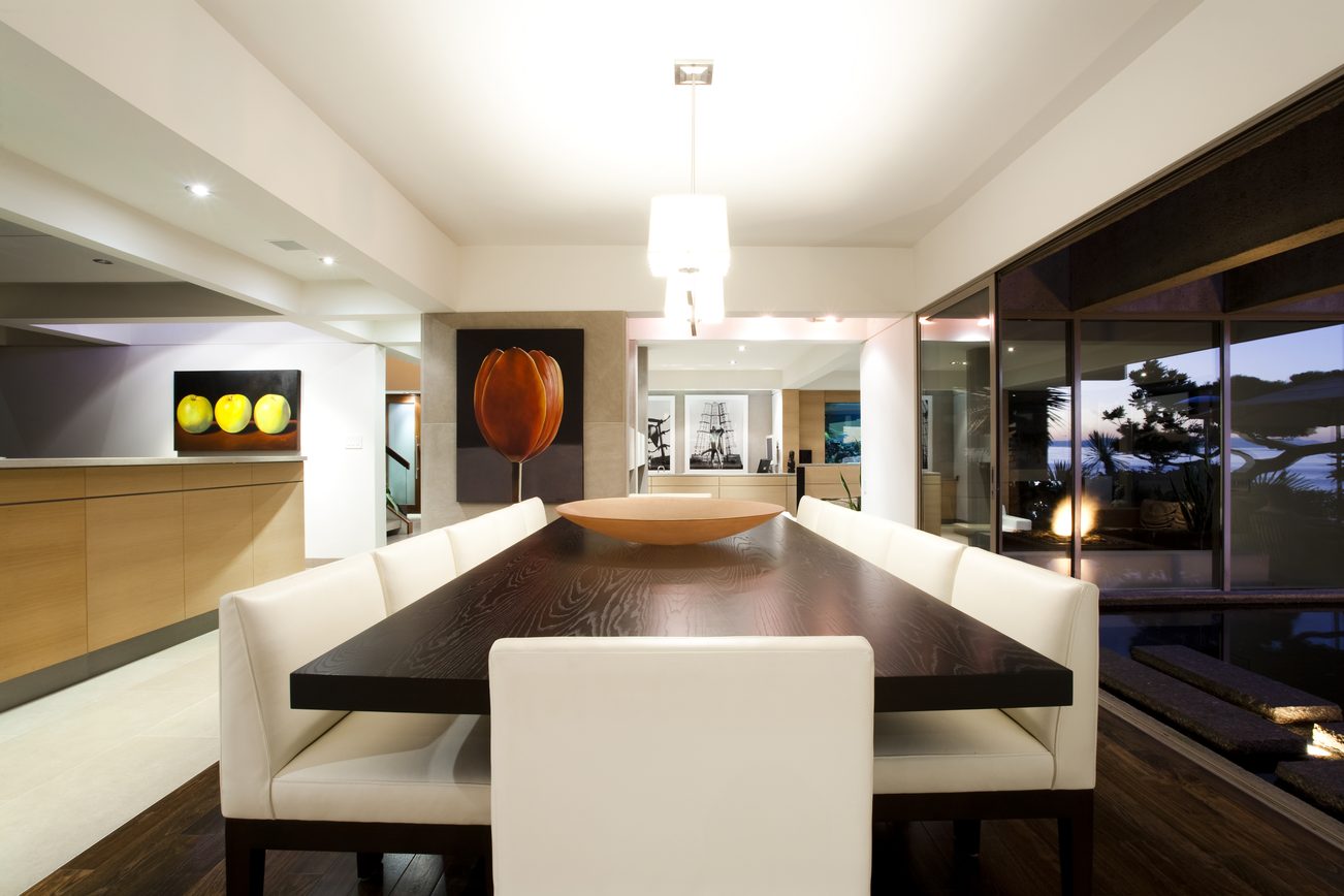 Modern dining room with sleek table, white chairs, and large windows showing a city view. - 2898 Bellevue Avenue, West Vancouver