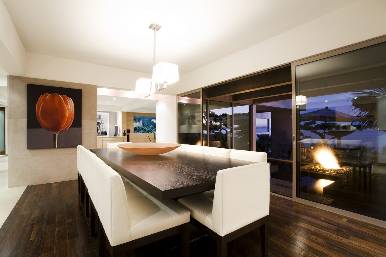 Modern dining room with sleek table, white chairs, and large sliding glass doors leading to an outdoor patio. - 2898 Bellevue Avenue, West Vancouver
