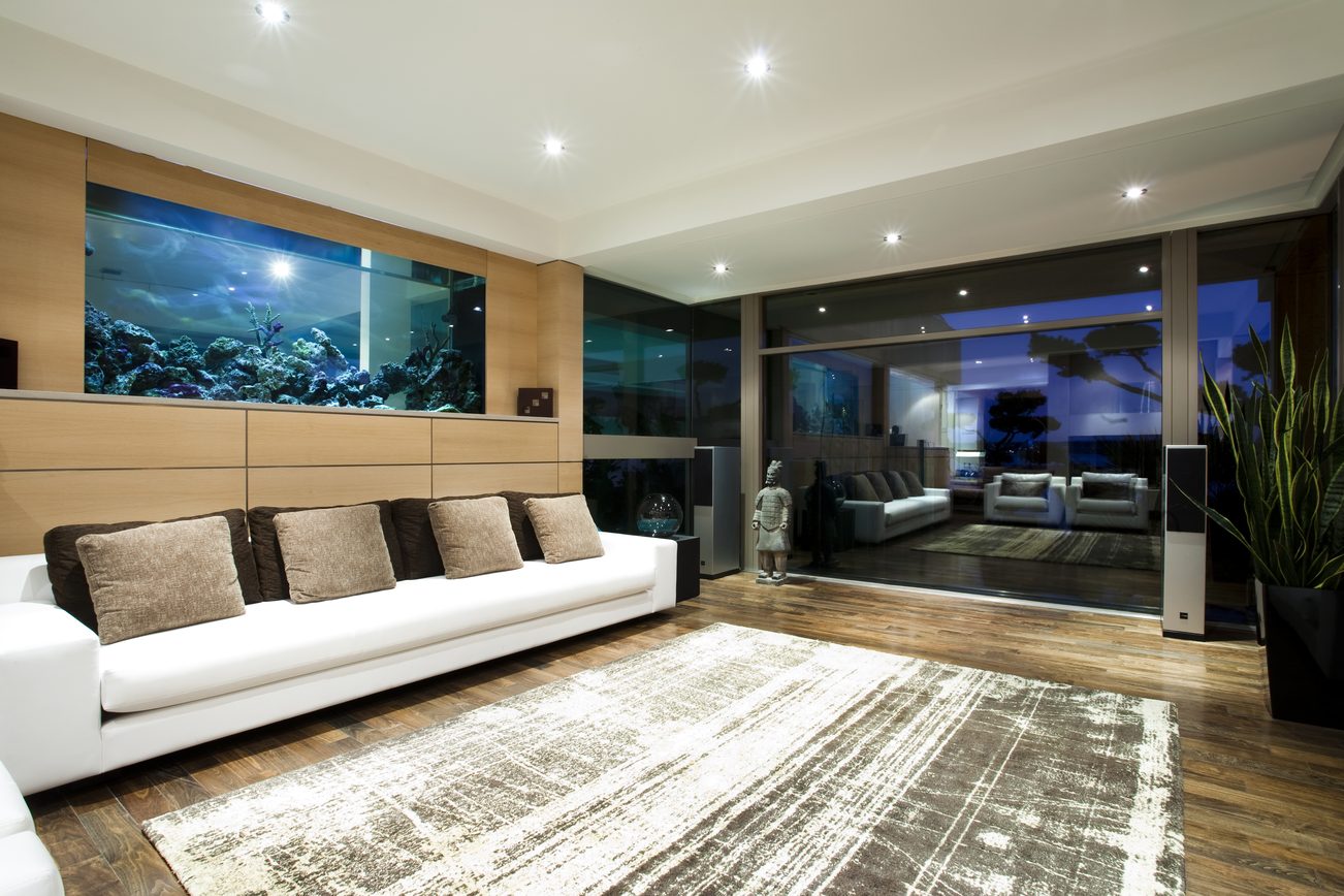 Bright living room with large aquarium wall, modern white sectional, hardwood floors, and city view. - 2898 Bellevue Avenue, West Vancouver