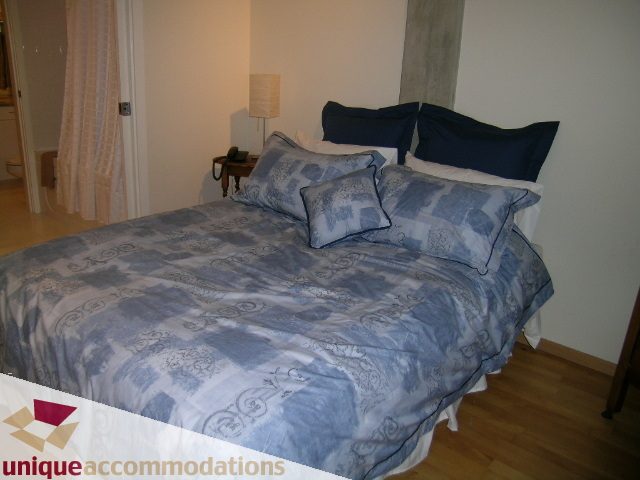 Spacious 2-bedroom condo with hardwood floors and a neatly made bed with blue patterned bedding. - PH3  603 - 1155 Mainland, Vancouver Downtown