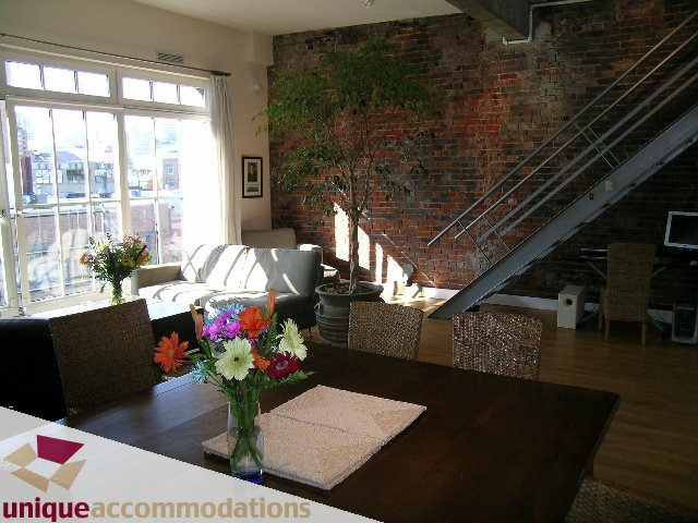 Furnished living room with exposed brick wall, wooden dining table, and city view through large windows.