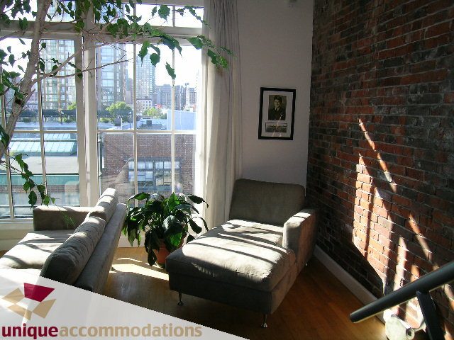 Bright living room with large windows, brick walls, and a city view. - PH3  603 - 1155 Mainland, Vancouver Downtown