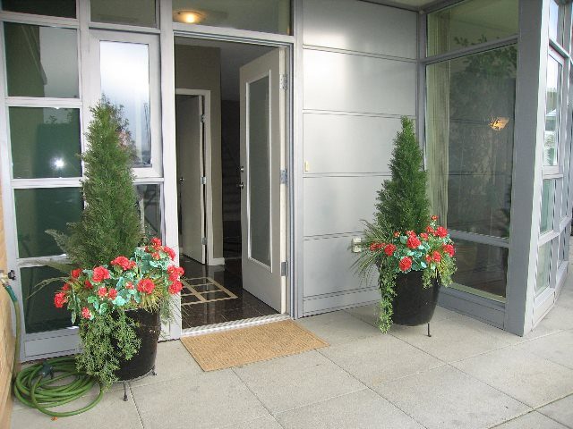 Furnished entryway with potted plants and a cozy mat, leading to a bright, open 2-bedroom + den townhouse.