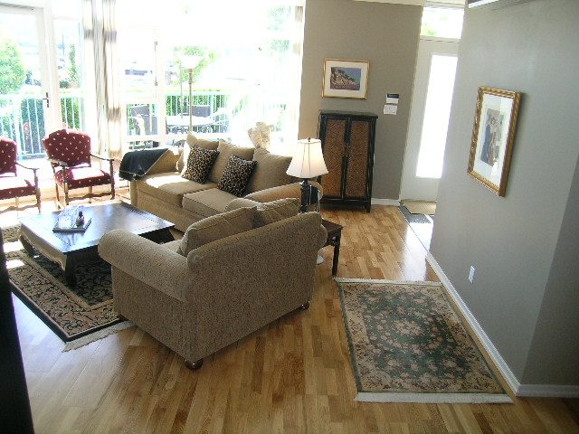 Spacious living room with hardwood floors, cozy beige furniture, and large windows offering a view of the marina.