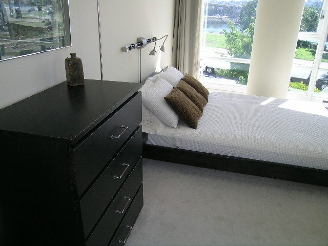 Spacious bedroom with modern furnishings, large windows offering a city view, and a sleek black nightstand.