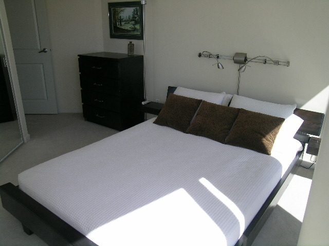 Spacious bedroom with two queen beds, brown throw pillows, and wall-mounted lights. - 1035 Marinaside Crescent, Vancouver Downtown