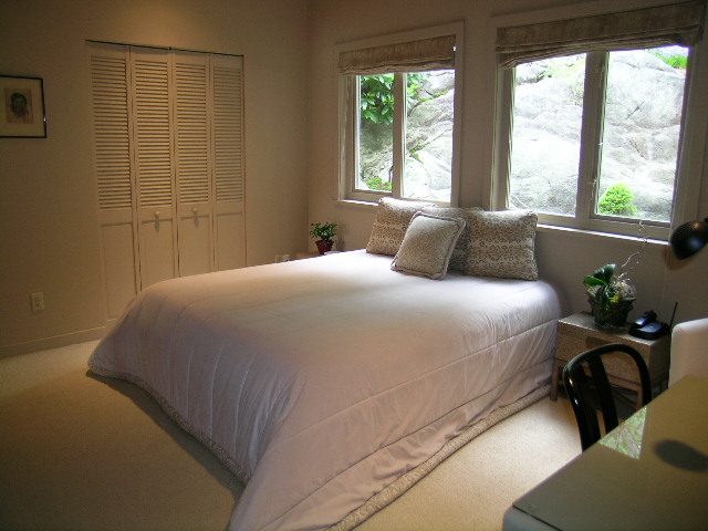 Spacious bedroom with large windows, white bedding, and a cozy ambiance. - 4527 Stonehaven Avenue, North Vancouver