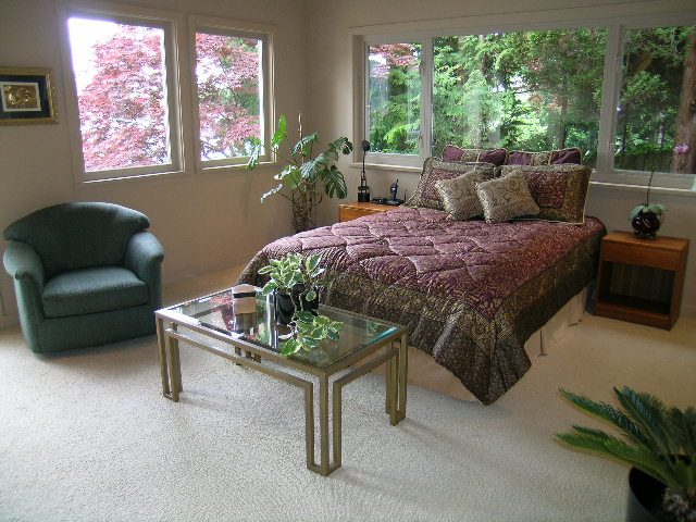 Bright living room with large windows, plush green armchair, and patterned sofa set. - 4527 Stonehaven Avenue, North Vancouver