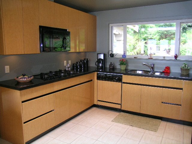 Bright kitchen with black countertops, wooden cabinets, and a window overlooking greenery. - 4527 Stonehaven Avenue, North Vancouver