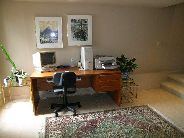 Living room with wooden desk, computer setup, and patterned rug. - 4527 Stonehaven Avenue, North Vancouver