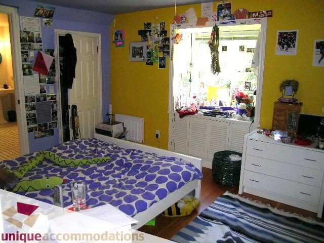 Bright bedroom with purple and blue patterned bedding, hardwood floors, and a large window. - 3664 Creery Ave., West Vancouver