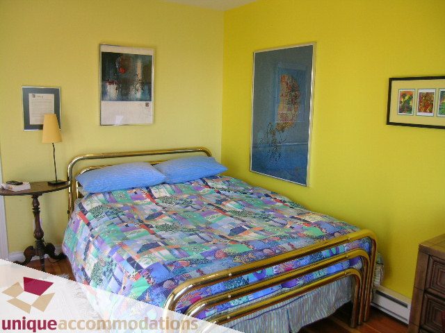 Bright bedroom with twin beds, colorful patchwork quilts, and yellow walls. - 3664 Creery Ave., West Vancouver