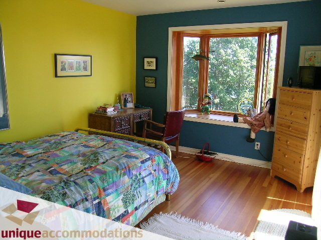 Bright bedroom with hardwood floors, patchwork quilt, and large window with city view. - 3664 Creery Ave., West Vancouver