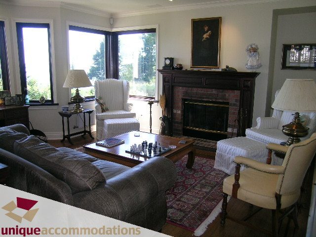 Living room with large windows, brick fireplace, and cozy seating. - 3664 Creery Ave., West Vancouver