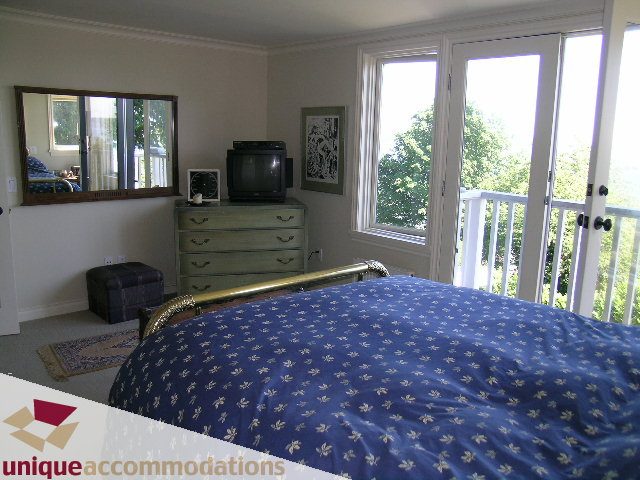 Bright bedroom with blue floral bedding, large window view, and dresser with mirror. - 3664 Creery Ave., West Vancouver