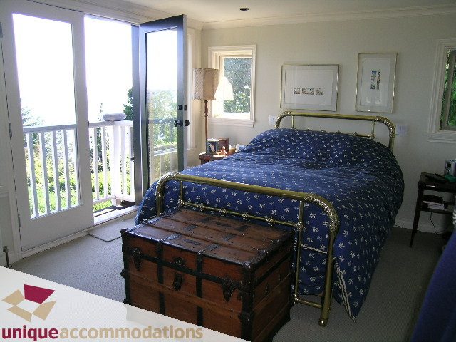 Bright bedroom with two twin beds, blue floral bedding, and a wooden trunk, overlooking a scenic view. - 3664 Creery Ave., West Vancouver
