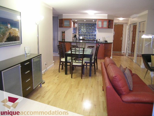 Furnished living room with hardwood floors, red leather couch, and kitchen with glass block backsplash.