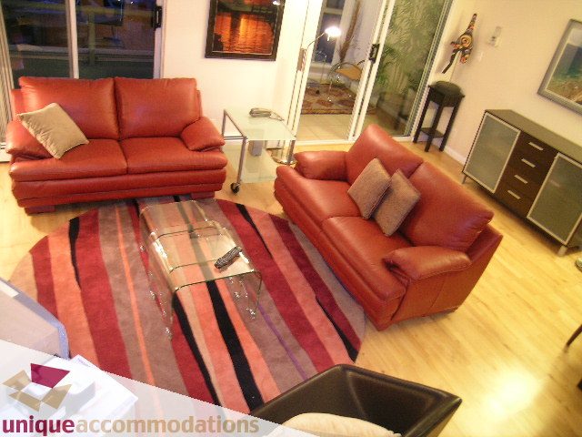Furnished living room with red leather furniture and striped rug, hardwood floors, and city view. - 322 - 1228 Marinaside Crescent, Vancouver Downtown