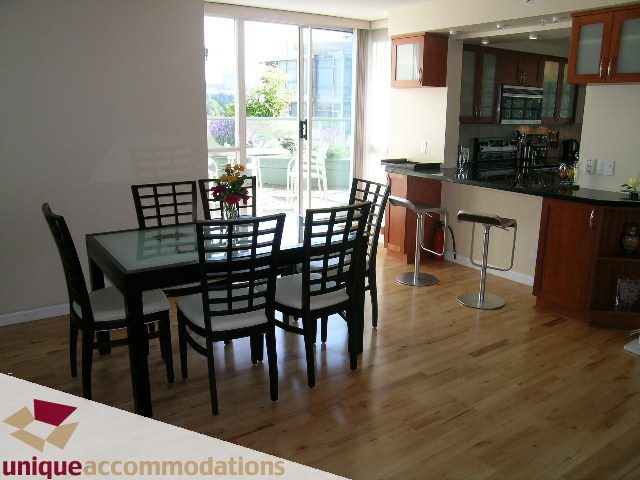 Modern dining area with hardwood floors, black chairs, and a city view through sliding doors. - 322 - 1228 Marinaside Crescent, Vancouver Downtown