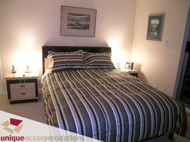 Furnished bedroom with striped bedding and nightstands, warm lighting. - 322 - 1228 Marinaside Crescent, Vancouver Downtown