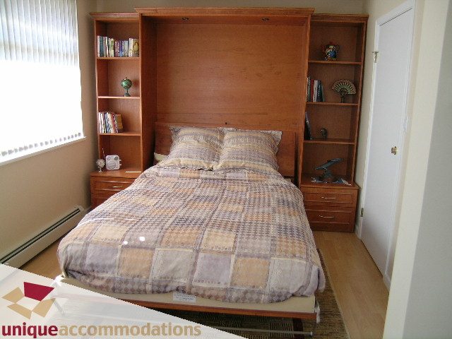 Furnished 2-bedroom + den townhouse with built-in Murphy bed, wooden shelves, and hardwood floors.