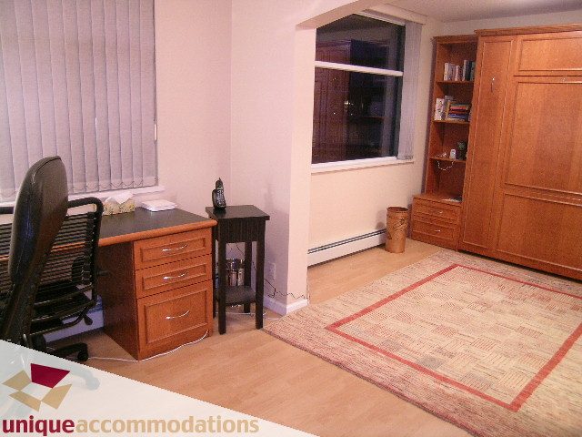 Bright living room with hardwood floors, wooden cabinets, and a large window. - 322 - 1228 Marinaside Crescent, Vancouver Downtown