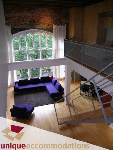 Open-concept living room with large windows, hardwood floors, and a cozy corner sofa. - 401 - 2525 Quebec Street, Vancouver East Side