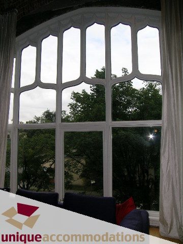 Furnished living room with large arched window, view of trees and sky. - 401 - 2525 Quebec Street, Vancouver East Side