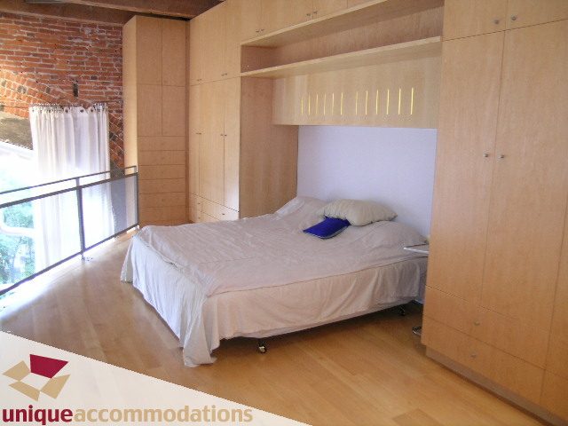 Furnished 1-bedroom with modern wooden furniture, hardwood floors, and a balcony view. - 401 - 2525 Quebec Street, Vancouver East Side