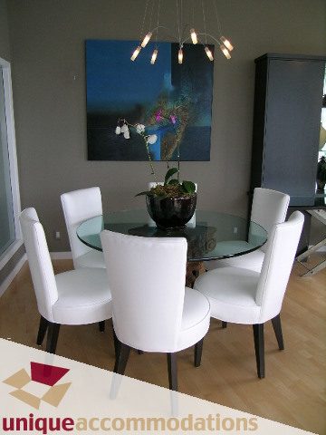 Furnished dining area with white chairs and a glass table, modern chandelier, hardwood floors. - 2502 - 1077 Marinaside Crescent, Vancouver Downtown