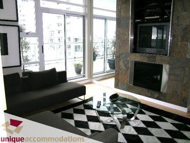 Furnished living room with black and white checkered rug, large windows, city view, and stone fireplace.