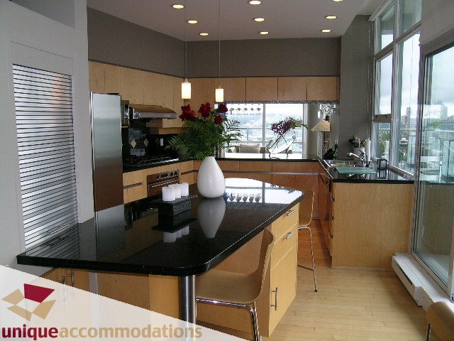Furnished kitchen with modern black countertops, hardwood floors, and a city view. - 2502 - 1077 Marinaside Crescent, Vancouver Downtown