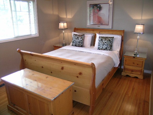 Furnished 2-bedroom suite with wooden sleigh bed, hardwood floors, and bedside lamps. - 470 Ellis Street, North Vancouver