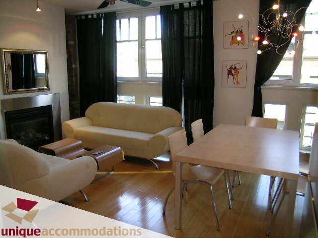 Furnished living room with hardwood floors and a fireplace, featuring a dining area with modern chairs and a large window...