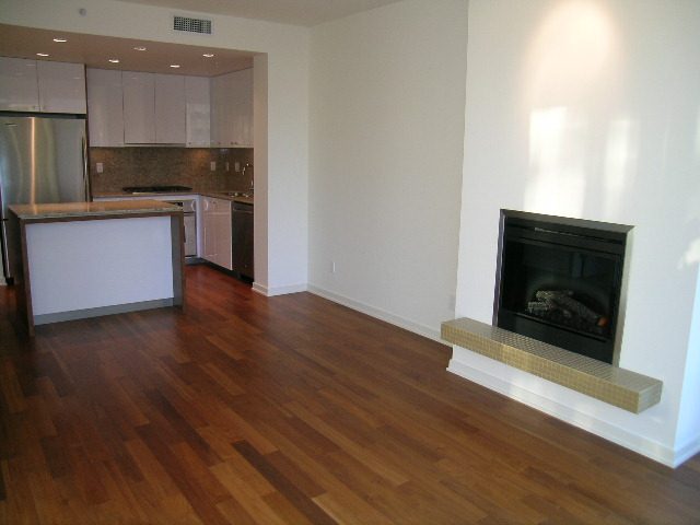 Bright kitchen with granite countertops and hardwood floors, leading to a cozy living area with a fireplace.