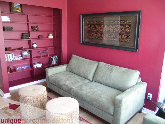 Furnished living room with red walls, bookshelf, and patterned ottoman. - 3607 - 1033 Marinaside Crescent, Vancouver Downtown