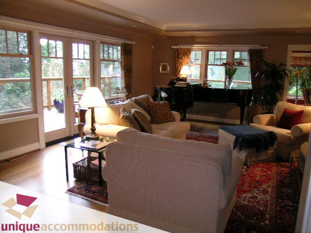 Spacious living room with large windows, hardwood floors, and a cozy sofa setup. - 4497 Marine Dr., West Vancouver