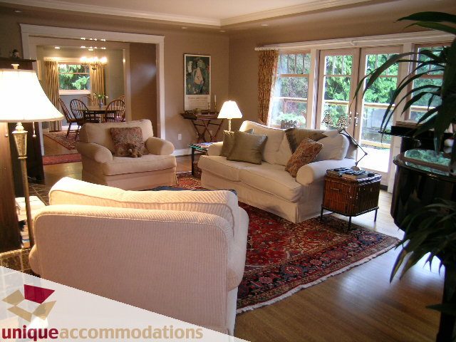 Spacious living room with hardwood floors, large windows, and a cozy sofa set. - 4497 Marine Dr., West Vancouver