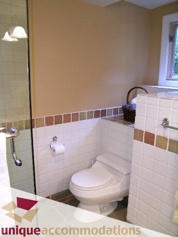 Bright bathroom with white tiles and a window, featuring a toilet and a sink with a mirror. - 4497 Marine Dr., West Vancouver