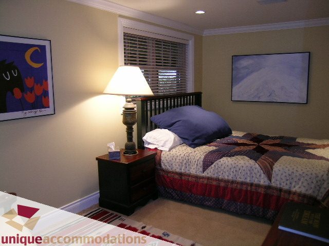 Bright bedroom with twin beds, patterned bedding, and a lamp. - 4497 Marine Dr., West Vancouver