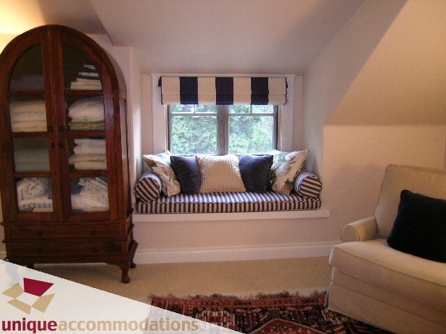 Bright sitting area with striped cushions and armoire, natural light from window. - 4497 Marine Dr., West Vancouver