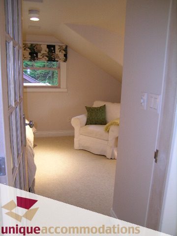 Bright attic bedroom with cozy white furniture, natural light, and a window view. - 4497 Marine Dr., West Vancouver