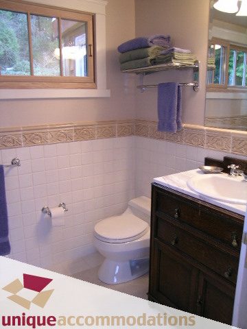 Furnished bathroom with white tile, wooden vanity, and window view. - 4497 Marine Dr., West Vancouver