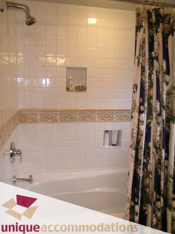 Bathroom with white tile walls, decorative border, and floral shower curtain. - 4497 Marine Dr., West Vancouver