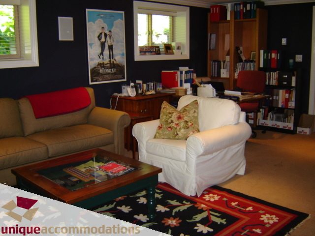 Living room with cozy furniture, bookshelves, and a colorful rug. - 4497 Marine Dr., West Vancouver