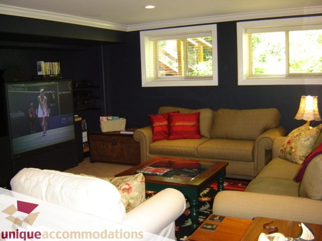 Living room with large sectional sofa, flat-screen TV, and natural light from windows. - 4497 Marine Dr., West Vancouver