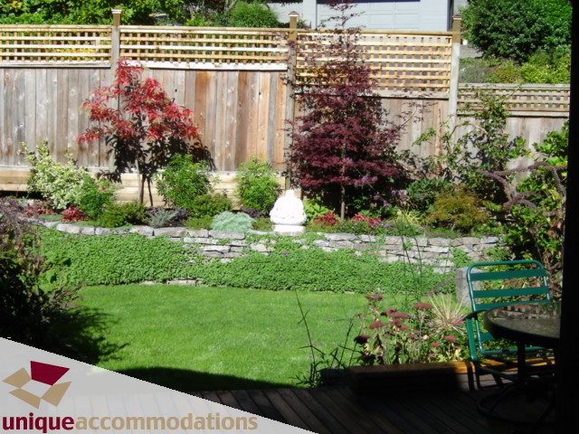 Furnished backyard with stone pathways, colorful shrubs, and wooden deck. - 4497 Marine Dr., West Vancouver